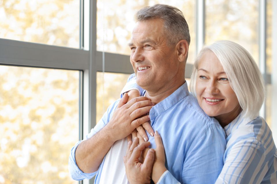 Smiling older couple standing by a sunny window
